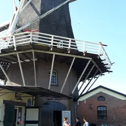 Bakhuismolen met bakstenen onderbouw en houten draaidak, witte reling zichtbaar, onderdeel van kringloopwinkel De Olde Bakker