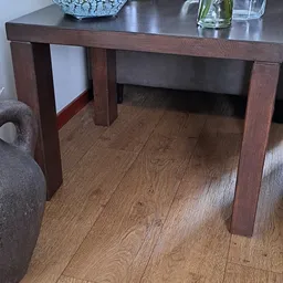 Onderaanzicht van een houten tafel met donkerbruin blad en poten, op houten vloer