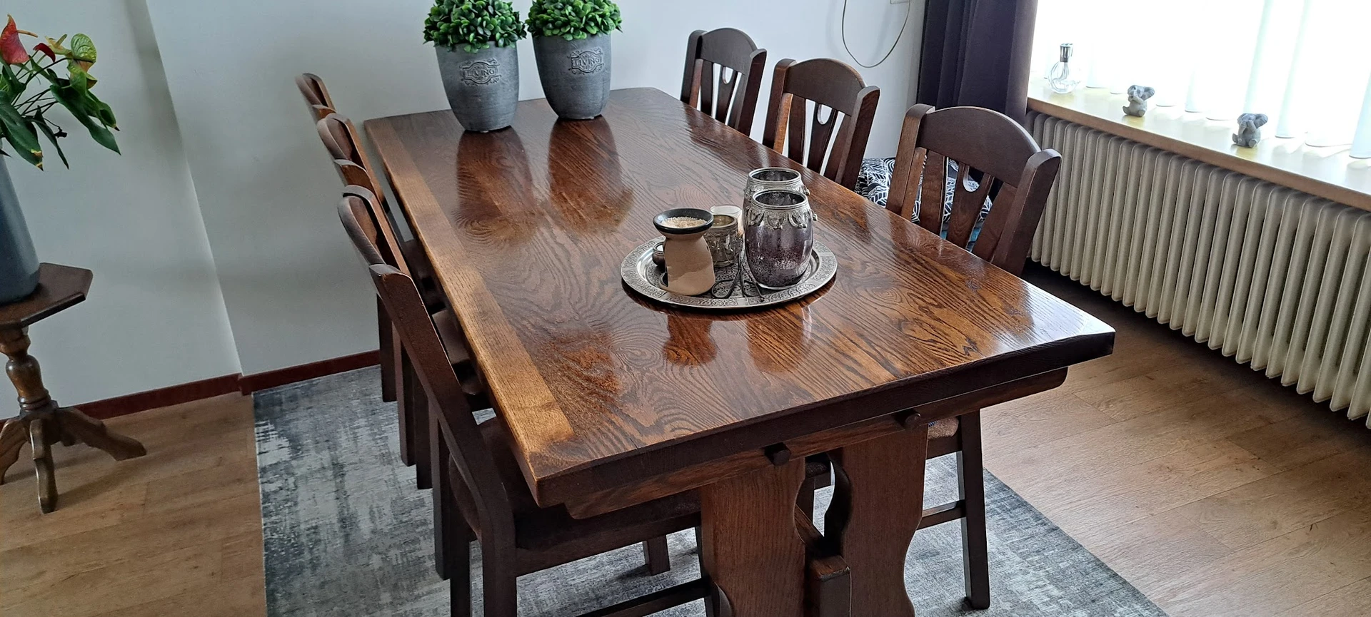 Houten eettafel met zes stoelen, twee potplanten en decoratieve objecten op tafelblad