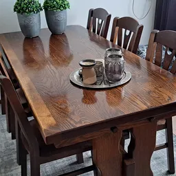 Houten eettafel met zes stoelen, twee potplanten en decoratieve objecten op tafelblad