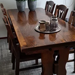 Donkerbruin houten eettafel met stoelen en een zwart dienblad met glazen potjes erop