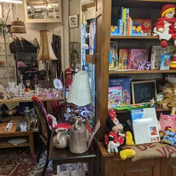 Winkelvloer met stellingen vol speelgoed, boeken en decoratieve artikelen, waaronder poppen, dominostenen en kinderspullen