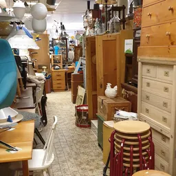 Binnenzicht van kringloopwinkel met houten meubels, kasten, stoelen en diverse spullen langs de wanden en gangpad