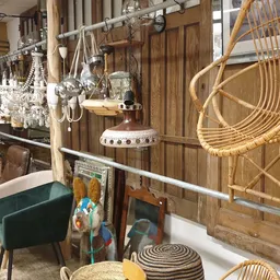 Winkelinterieur met diverse meubels en huishoudartikelen: rieten stoelen, groene fauteuil, houten kasten, hangende lampen en 