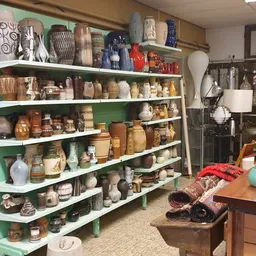 Groene stellingen volgeladen met aardewerk, vazen, servies en decoratieve huishoudartikelen