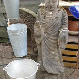 Stenen tuinbeelden en kunststof emmers op een kringloopwinkel-terras