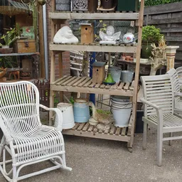 Houten stellingkast met diverse huishoudelijke artikelen, emmers, dozen en plantenpotten, met witte tuinstoelen ernaast