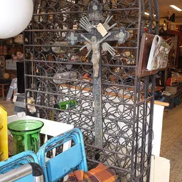 Decoratief metalliek scherm met kruismotief en groene vaas op witte tafel in kringloopwinkel
