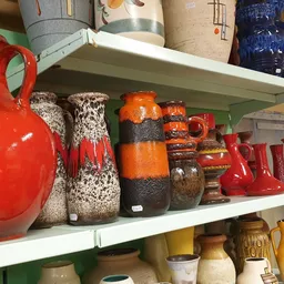 Witte stellingen met vintage en tweedehands huishoudelijke artikelen: rode kannen, keramische potten, vazen en decoratieve it