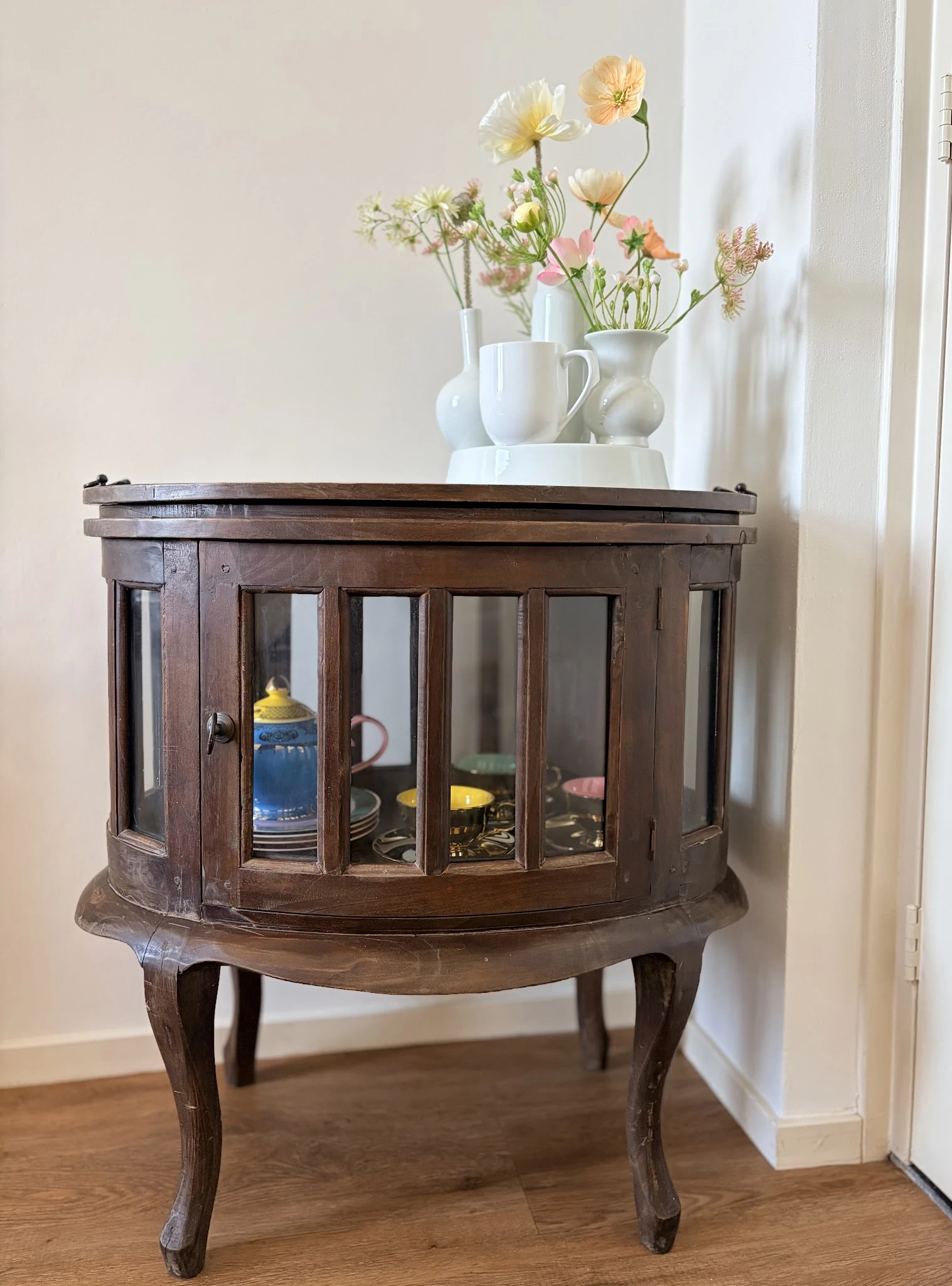 Houten vitrinekast met glazen deuren en glas-in-lood patronen, gevuld met serviesgoed en decoratieve items