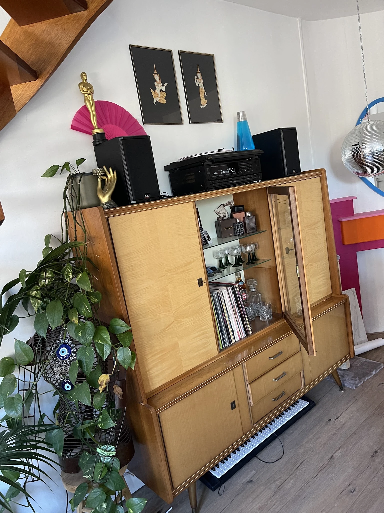 Vintage houten wandkast met glazen deuren en opbergvakken, gevuld met decoratieve items en dvd's