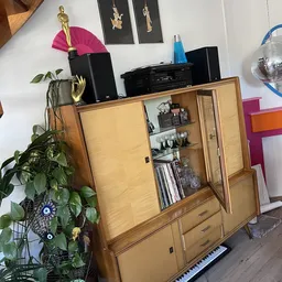 Vintage houten wandkast met glazen deuren en opbergvakken, gevuld met decoratieve items en dvd's