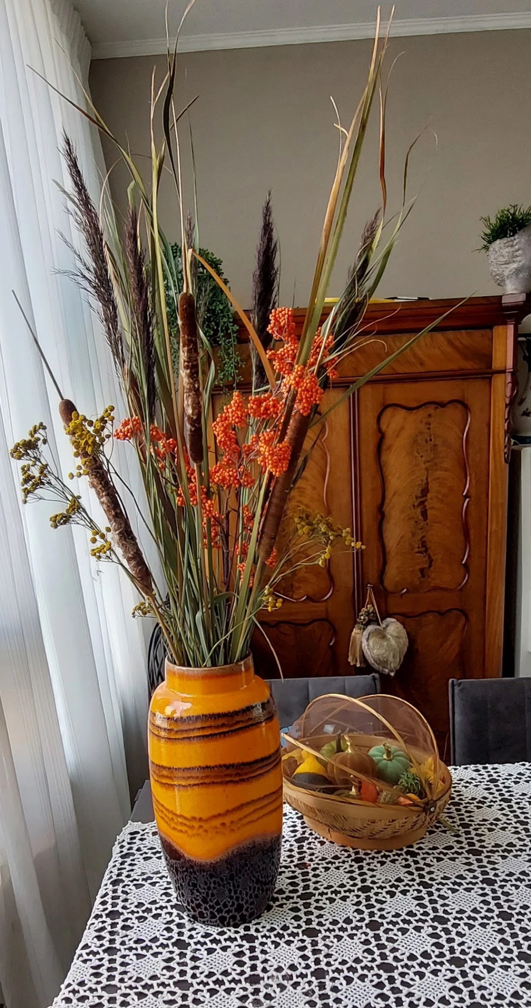 Geel aardewerk vaasje met droogbloemen en decoratieve takken in oranje en groen.