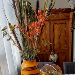Geel aardewerk vaasje met droogbloemen en decoratieve takken in oranje en groen.