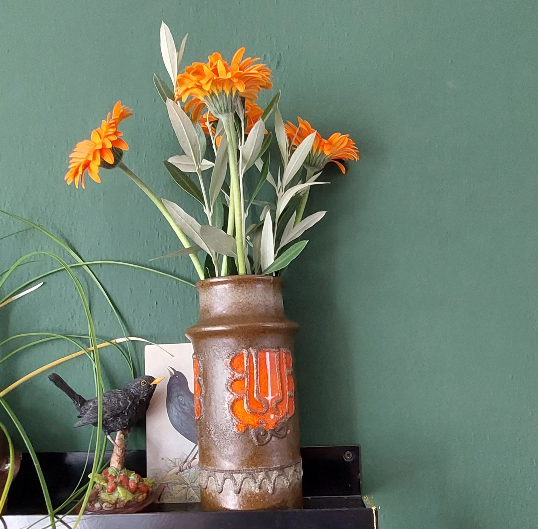Bruine vaas met oranje bloemen en groen blad tegen groene achtergrond