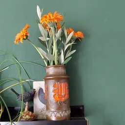 Bruine vaas met oranje bloemen en groen blad tegen groene achtergrond