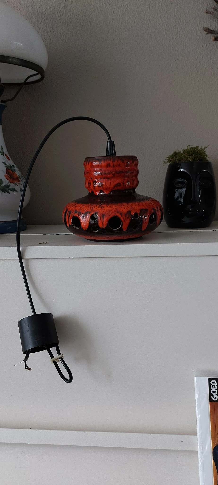 Rode glazen vaas met zwarte decoratieve gaten op een witte plank, naast zwarte vazen