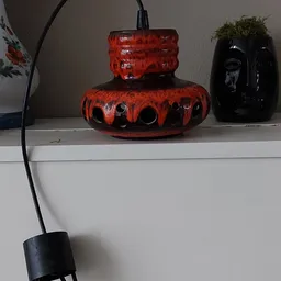 Rode glazen vaas met zwarte decoratieve gaten op een witte plank, naast zwarte vazen
