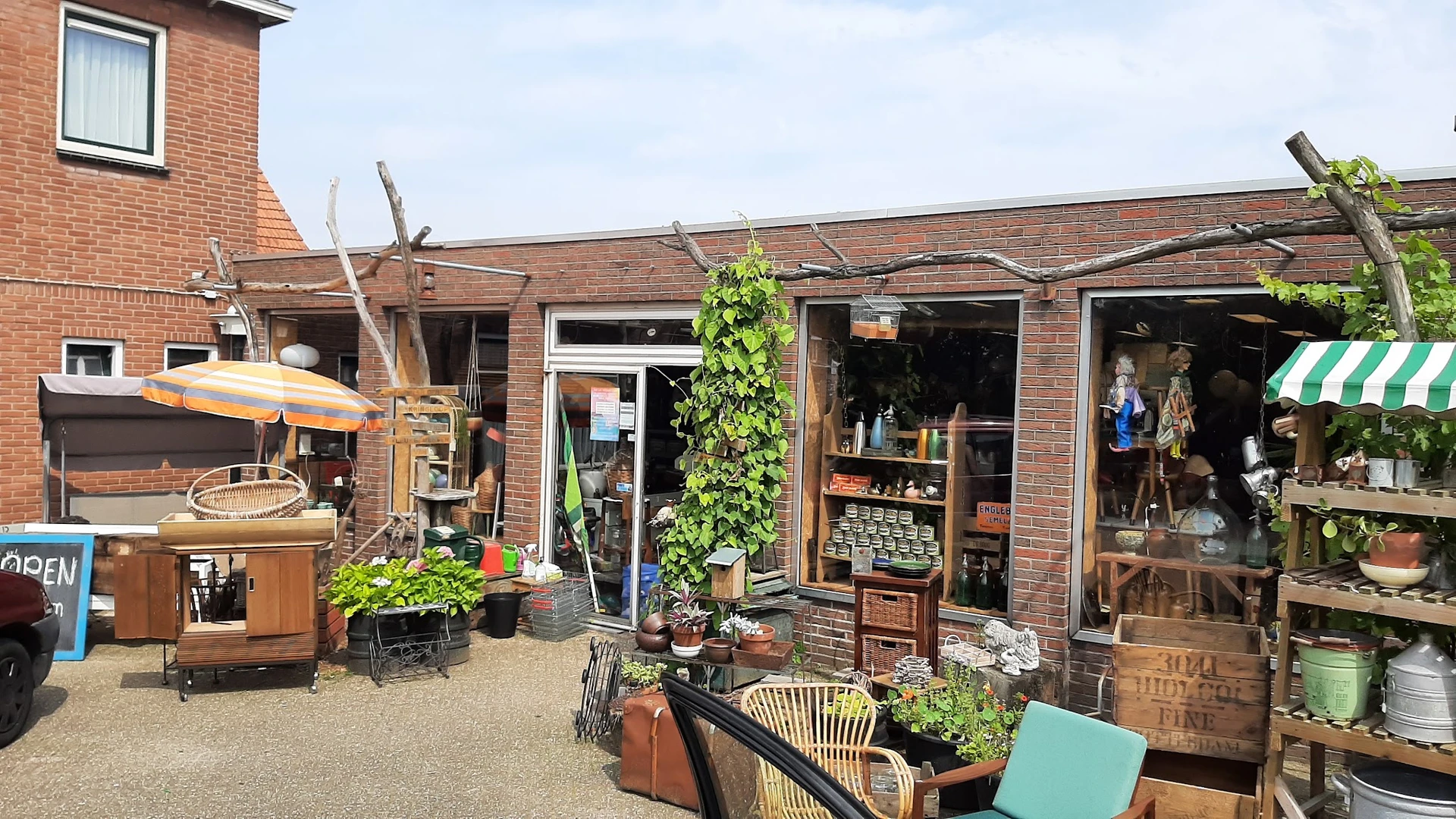 Voorkant kringloopwinkel met bakstenen gevel, etalageruiten en houten decoratieve elementen