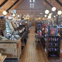 Ruim interieur van kringloopwinkel met houten vloer, stellingen met spullen, ronde hangende lampen en fauteuils op de voorgro