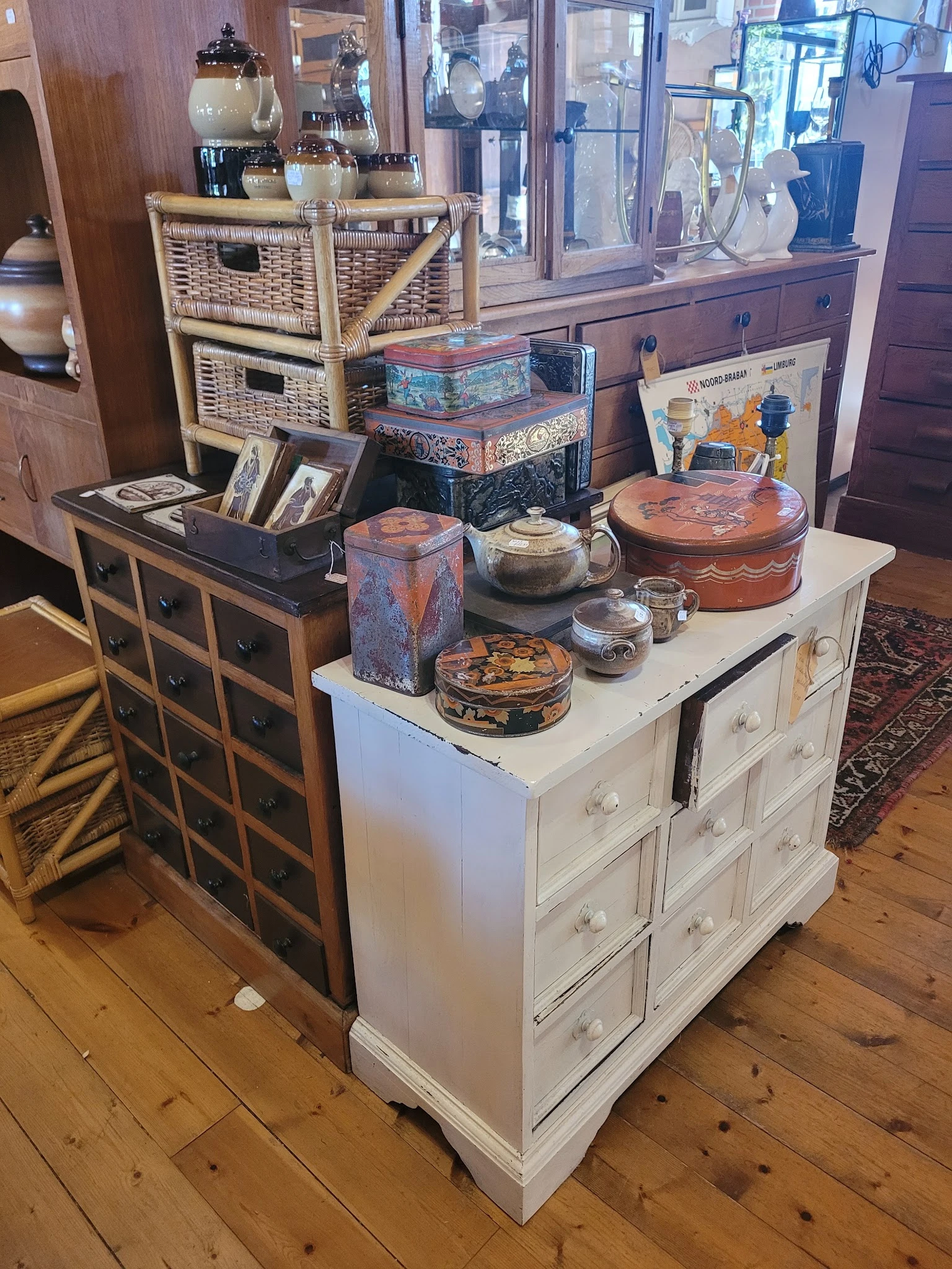 Witte en donkere commodes met decoratieve dozen, servies en huishoudspullen erop uitgestald