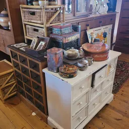 Witte en donkere commodes met decoratieve dozen, servies en huishoudspullen erop uitgestald
