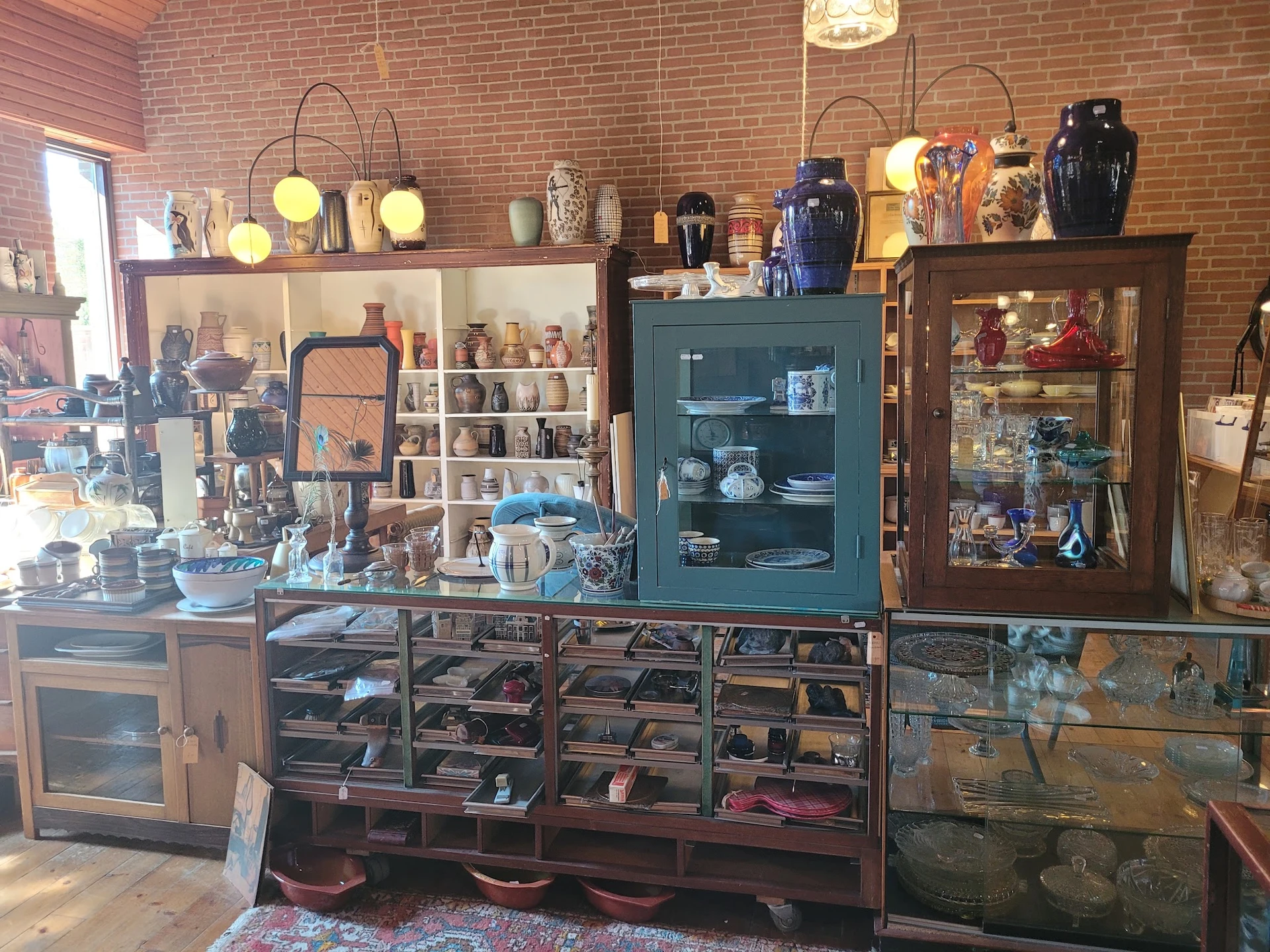 Winkelbinnenruimte met bakstenen muur, glazen vitrines, houten kasten en diverse antieke en decoratieve voorwerpen