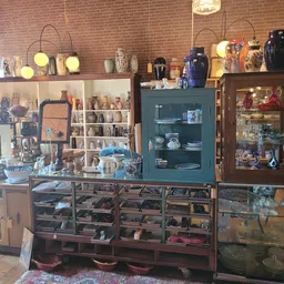 Winkelbinnenruimte met bakstenen muur, glazen vitrines, houten kasten en diverse antieke en decoratieve voorwerpen