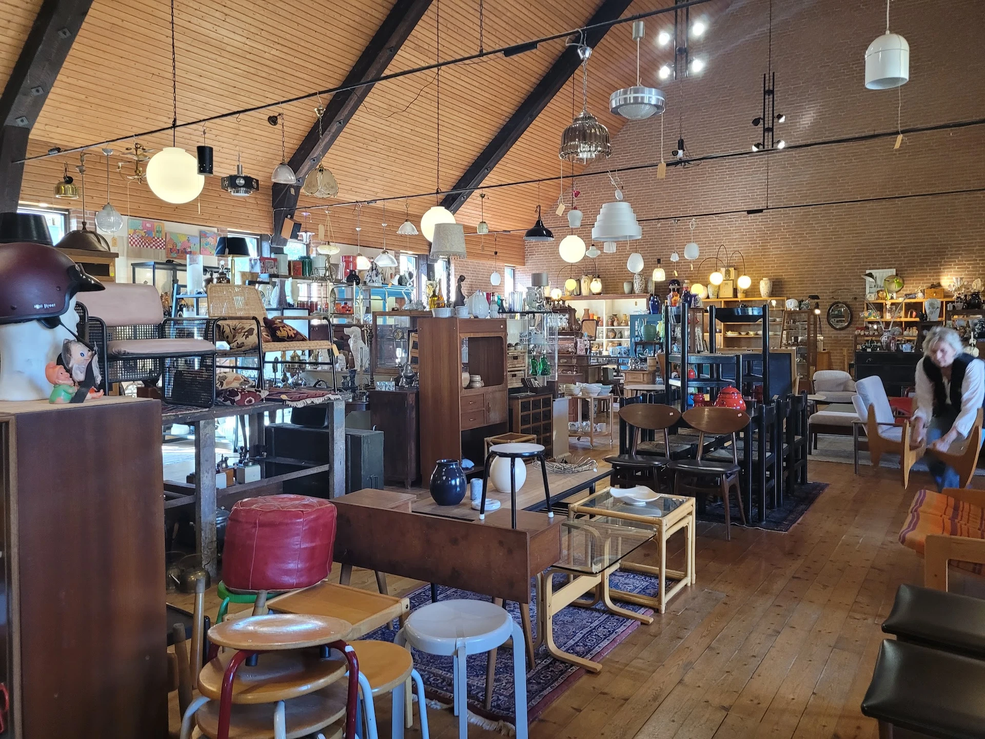 Ruim winkelinterieur met houten balkenplafond, diverse hang- en hanglampjes, meubels, stoelen en spullen uitgestald op stelli