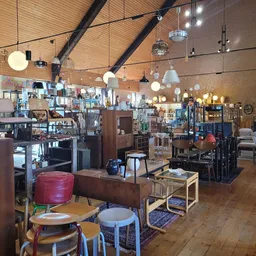 Ruim winkelinterieur met houten balkenplafond, diverse hang- en hanglampjes, meubels, stoelen en spullen uitgestald op stelli