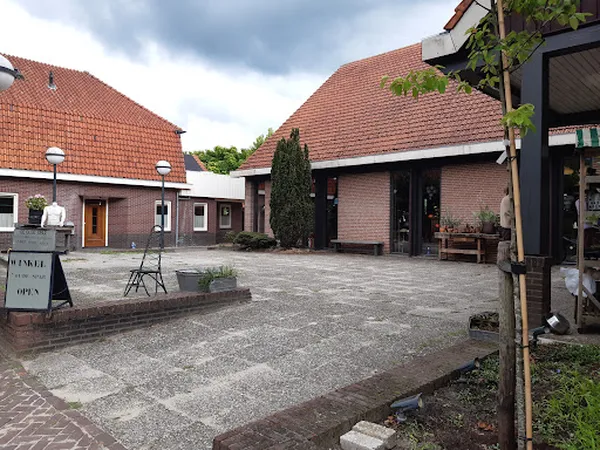 Voorzijde van kringloopwinkel met bakstenen gevels, rode daken en ingang, omgeven door bestrating en groen