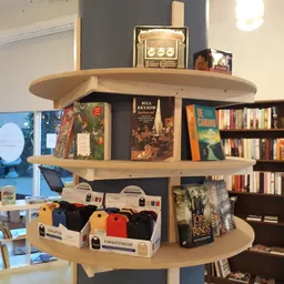 Winkelinterieur met houten displaykasten vol boeken, media en klein huishoudelijk spul