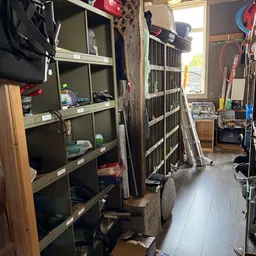 Smalle winkelgang met houten stellingen, stellagekasten en diverse spullen; zicht op ingang en winkelruimte