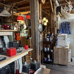 Winkelinterieur met houten stellingen, rode hanglampjes, decoratiespullen, blauwe keramiek, een blauwe geruite blouse en dive