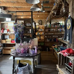 Winkelvloer met rond tafel vol paarse flesjes en producten, stellingen met spullen in houten kast op achtergrond, kleding han