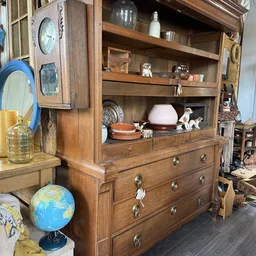 Houten kast met diverse spullen: serviesgoed, beeldjes, glazen, boeken en decoratieve items op meerdere planken en laden