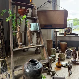 Verzameling vintage huishoudartikelen en decoratie, waaronder houten beelden, servies, kandelaars en koperen items op een wer