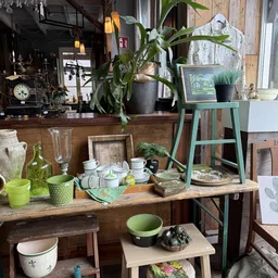 Tafelscène met servies, glazen, plantenpotten en decoratieve items in een kringloopwinkel