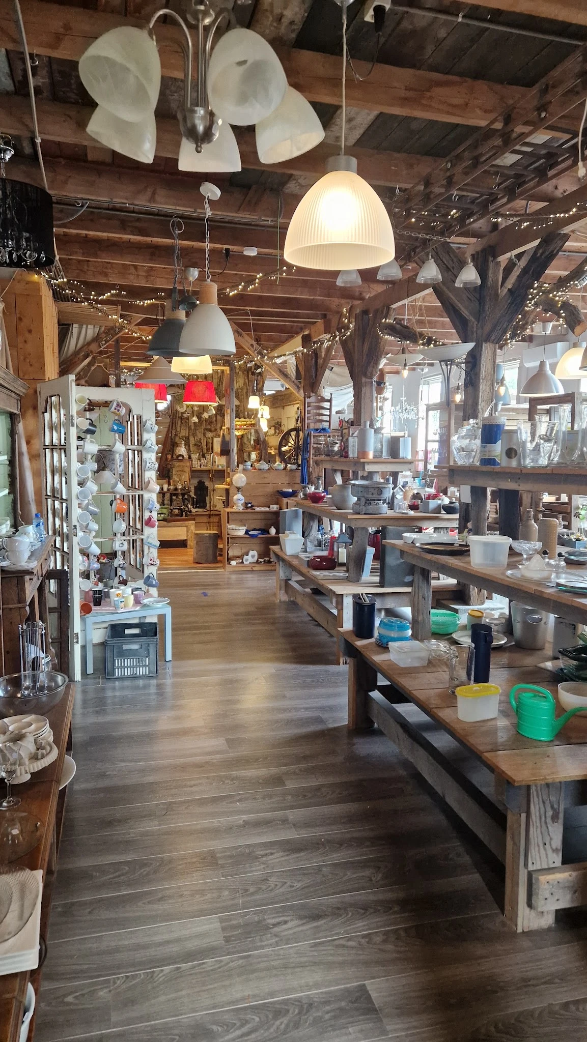 Binnenaanzicht van kringloopwinkel met houten balken, werkbanken, stellingen met spullen en hanglampen