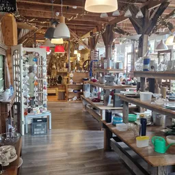 Binnenaanzicht van kringloopwinkel met houten balken, werkbanken, stellingen met spullen en hanglampen