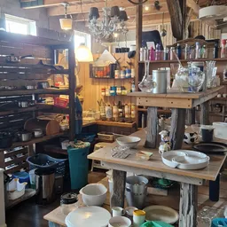 Winkelbinnenruimte met houten tafels, stellingen, huishoudartikelen en diverse spullen