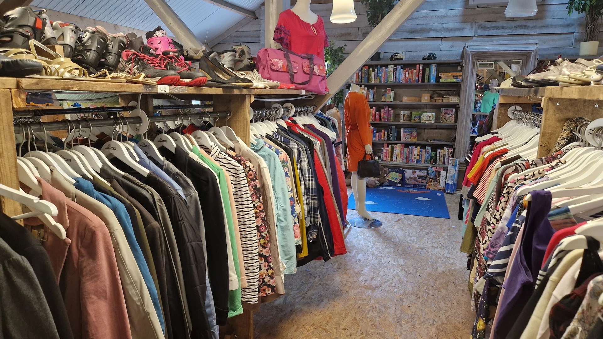 Ruim winkelinterieur met kledingrekken vol tweedehands kleding, boekenkasten en een blauwe mat op de grond