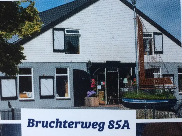 Witte kringloopwinkel met zwarte pui en ramen, adres Bruchterweg 85A zichtbaar op bord