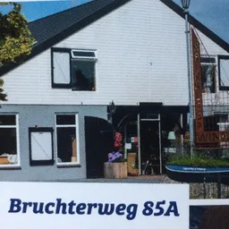 Witte kringloopwinkel met zwarte pui en ramen, adres Bruchterweg 85A zichtbaar op bord