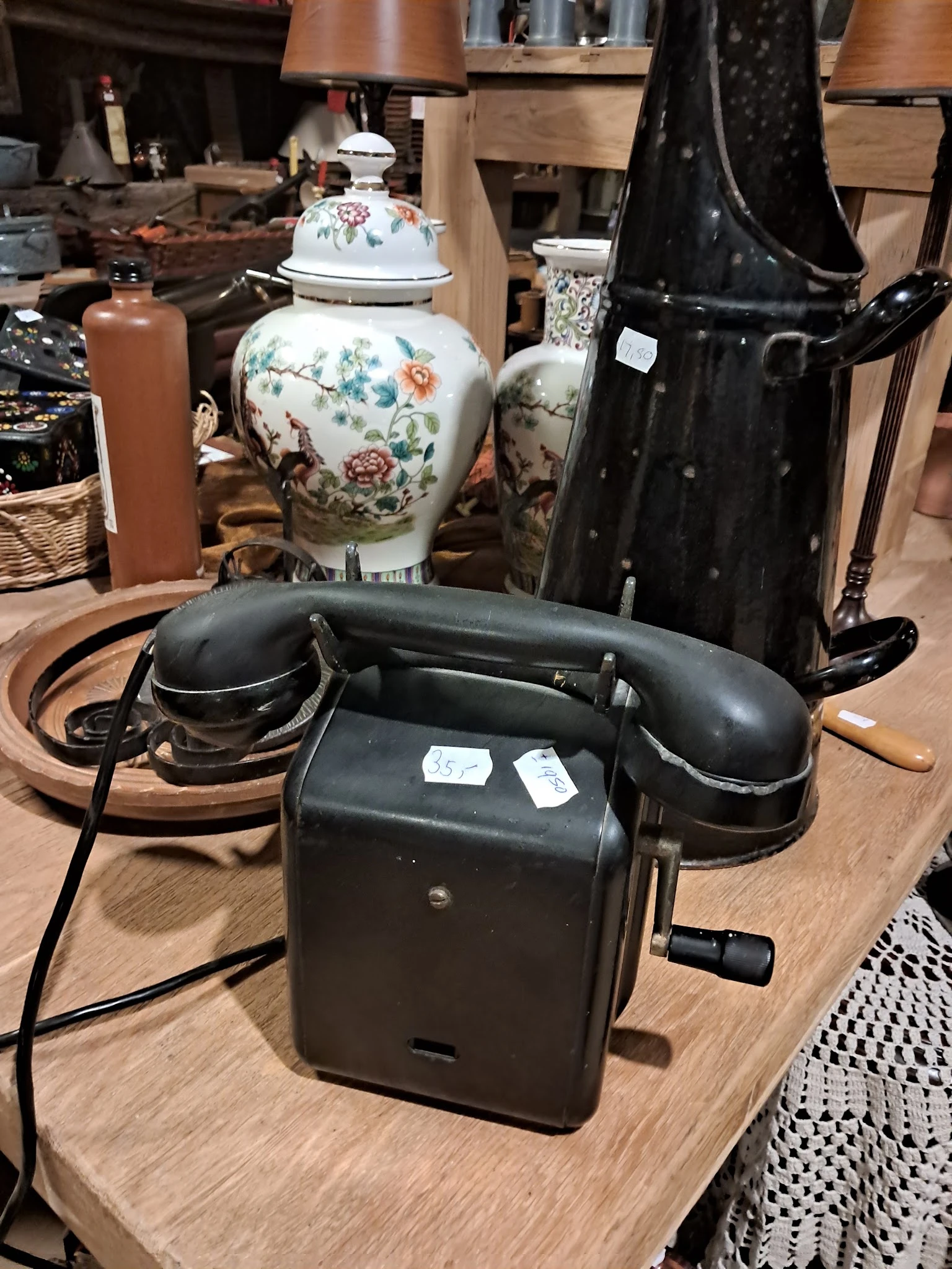 Vintage zwarte telefoon met draaischijf tussen andere antieke huishoudartikelen en decoratieve items