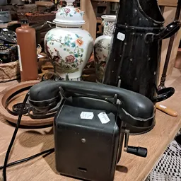 Vintage zwarte telefoon met draaischijf tussen andere antieke huishoudartikelen en decoratieve items