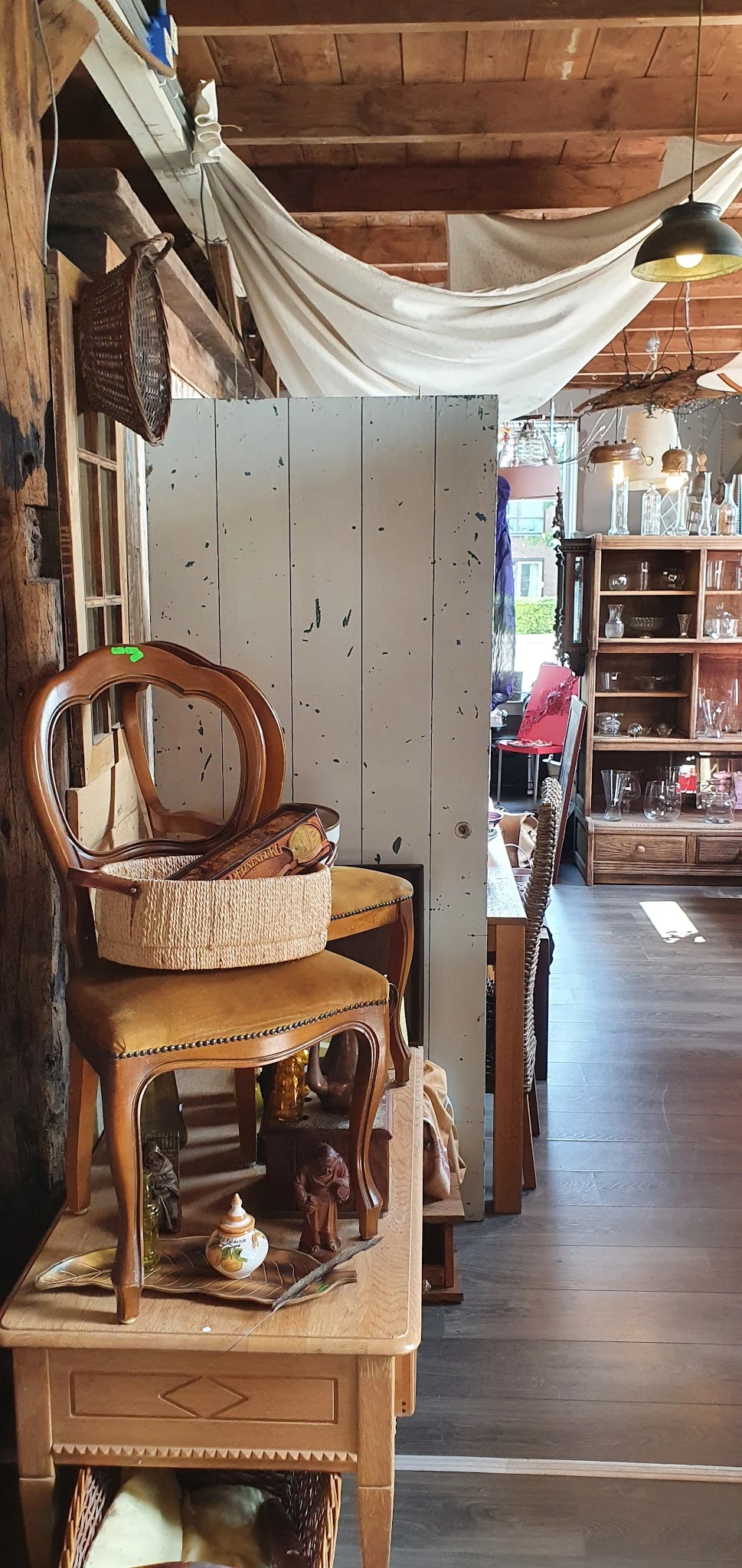 Houten stoelen en meubels met rieten mand en decoratieve items in kringloopwinkel