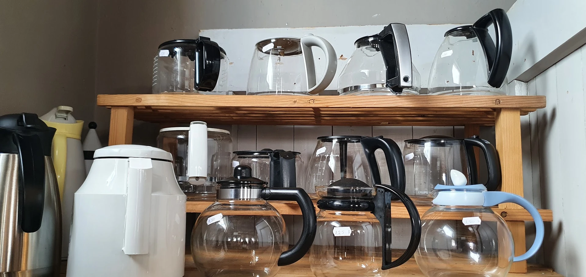 Houten rekken met diverse koffiezetapparaten en waterkokers, deels verpakt in doosjes