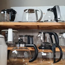 Houten rekken met diverse koffiezetapparaten en waterkokers, deels verpakt in doosjes