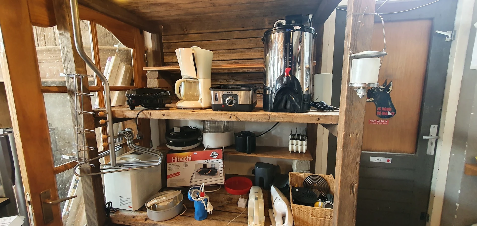 Houten stellingen met huishoudelijke apparaten en keukengerei zoals koffiezetapparaten, mengpannen en andere tweedehands spul